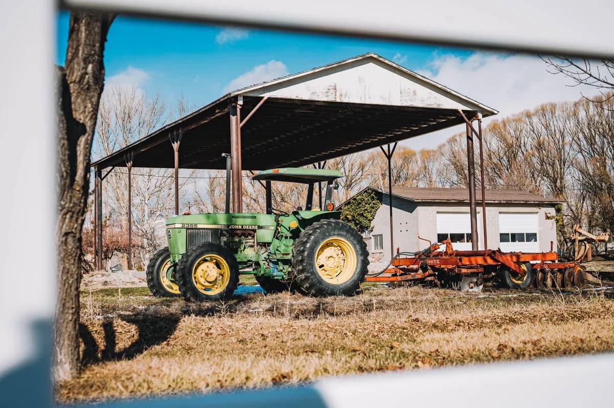BookNoFees Ukážkový obrázok: Zelený traktor pod otvoreným poľnohospodárskym prístreškom