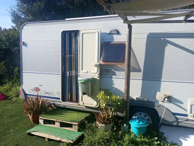 BookNoFees: ubytovanie, El Palmar De Vejer – Exteriér retro karavanu s otvorenými dverami, markízou a kvetinami v kvetináčoch na trávniku