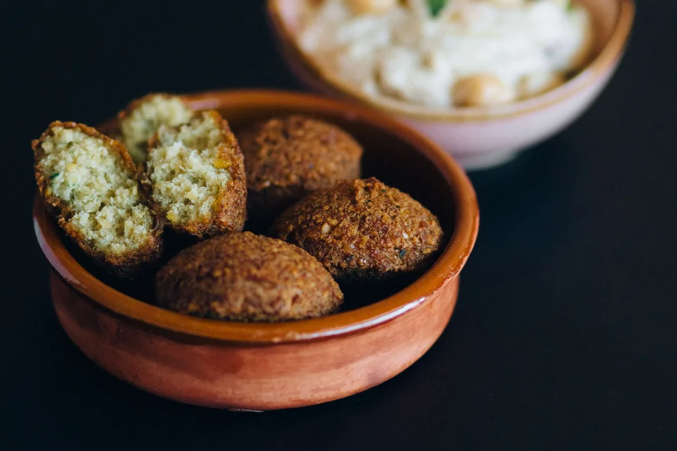 BookNoFees: Ukážková fotografia: Falafelové guľôčky, vrátane rozrezaného kúska, v miske s hummusom v pozadí